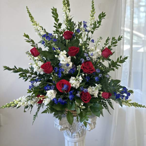 Tall arrangement of red roses, white snapdragons, and blue flowers in a basket