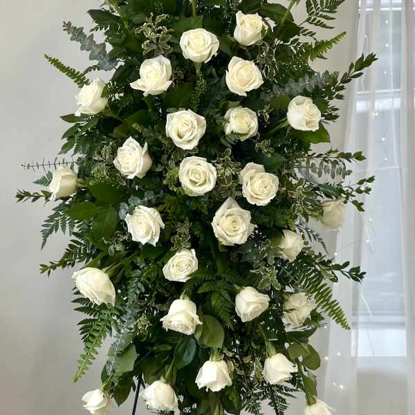 Tall standing arrangement of white roses and greenery on a black easel