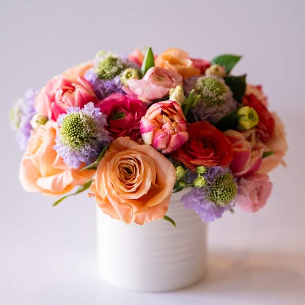 Mixed bouquet of peach, pink, and purple flowers in a white vase