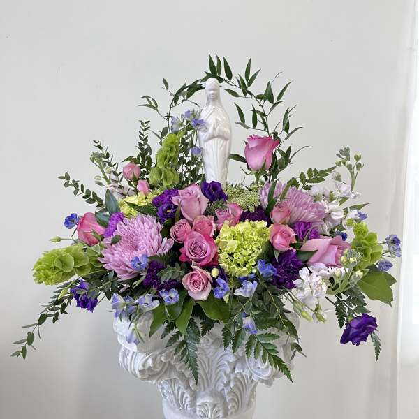 Pink and purple floral arrangement in a white pedestal urn with a statue