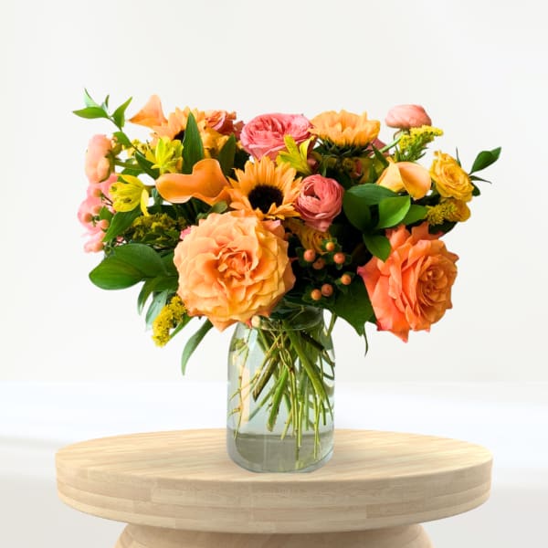 Mixed orange and pink flowers arranged in a clear glass vase
