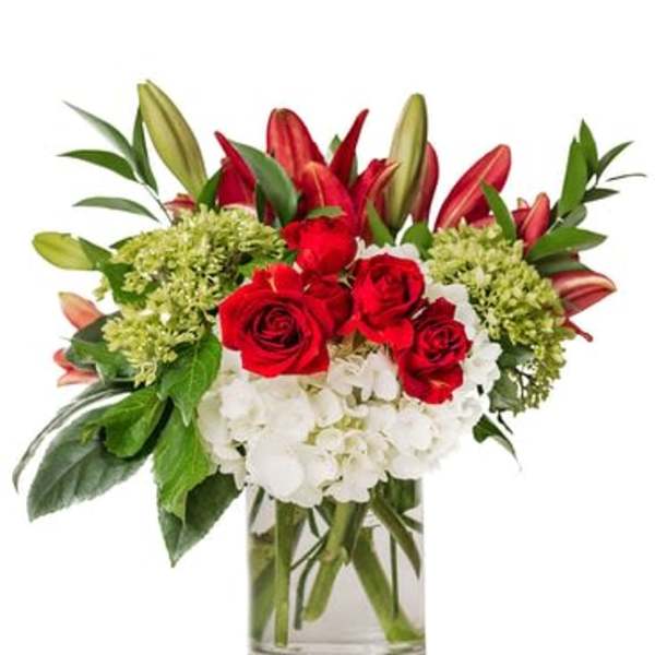 Red roses and lilies arranged with white hydrangeas in a glass vase