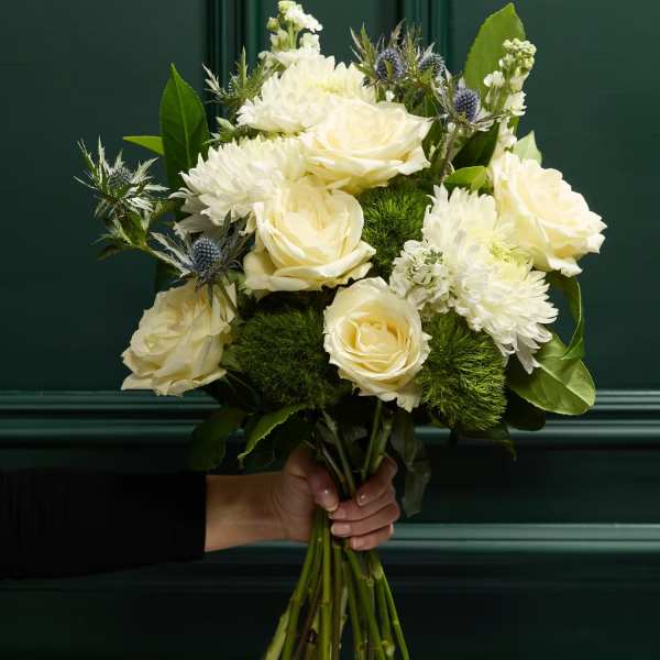 Handheld bouquet of white roses and white chrysanthemums with blue thistle accents