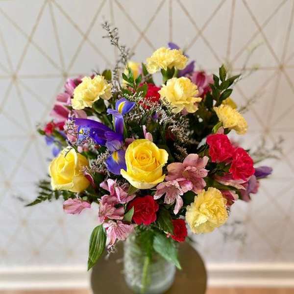 Mixed bouquet of roses, carnations, and purple flowers in a glass vase