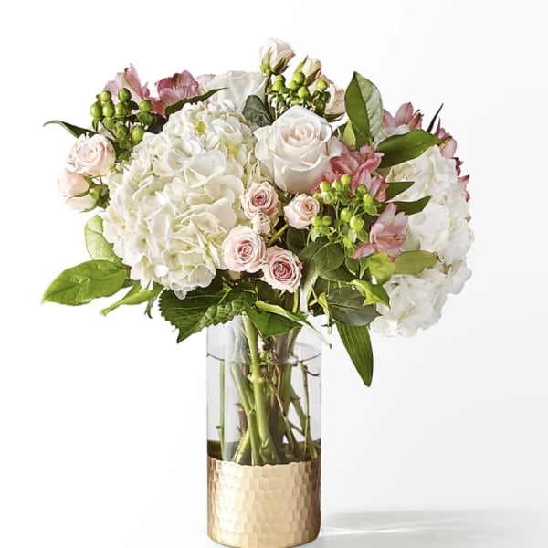White hydrangeas and pale pink roses in a glass vase with a gold base