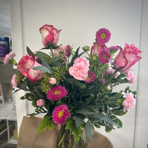 Bouquet of pink roses, carnations, and purple daisies in a glass vase