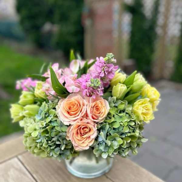 Bouquet of peach roses, pink blooms, and green hydrangeas in a glass vase