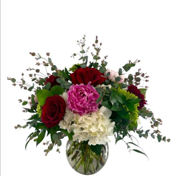 Bouquet of red roses, pink peonies, and white hydrangeas in a glass vase