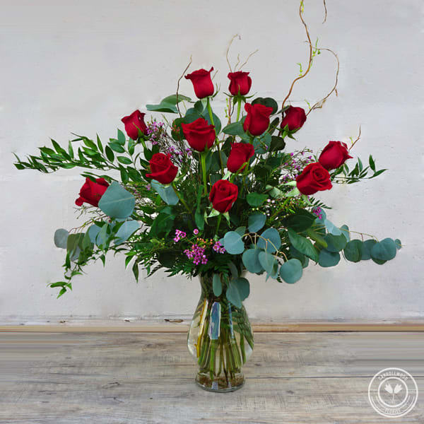 Red roses arranged in a clear glass vase with eucalyptus and filler flowers