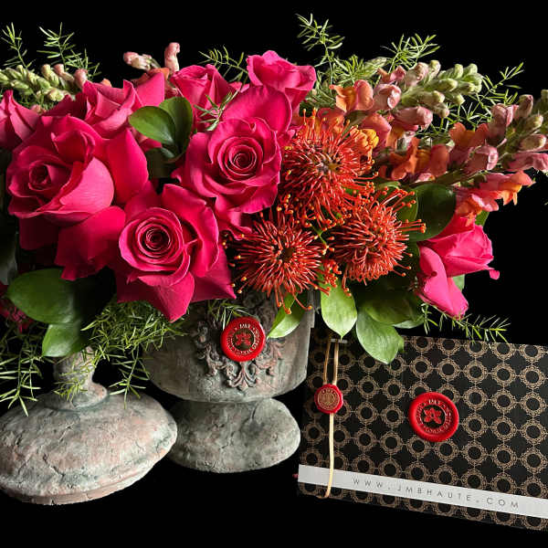 Hot pink roses and orange pincushion blooms in a stone vase with a patterned card