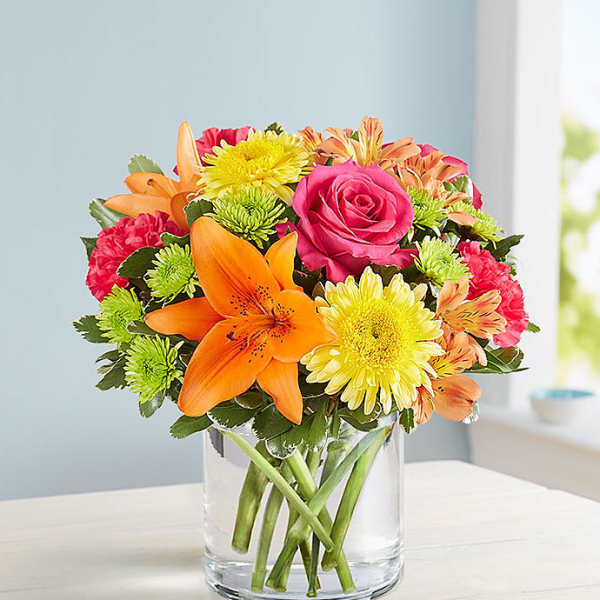 Bouquet of orange lilies, pink roses, and yellow daisies in a clear glass vase