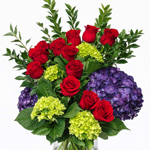 Red roses and purple hydrangeas in a clear glass vase