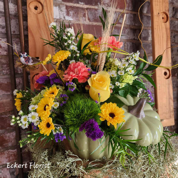 Mixed flower arrangement in a pumpkin-shaped container with yellow roses and daisies