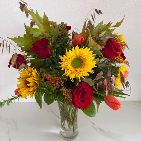 Bouquet of red roses, sunflowers, and orange tulips in a clear glass vase