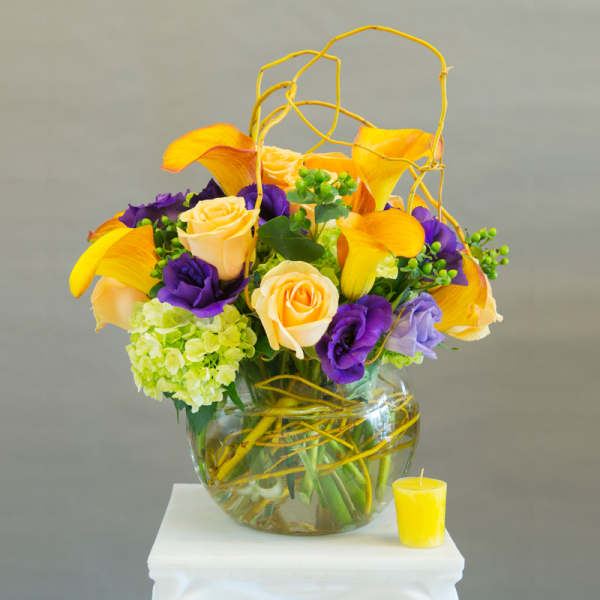Bouquet of yellow calla lilies, roses, and purple blooms in a glass vase