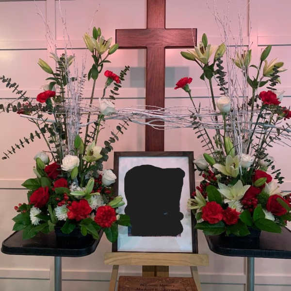 Symmetrical funeral floral display with red and white flowers around a framed photo and cross