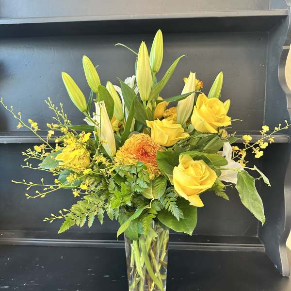 Yellow roses and lilies arranged in a clear glass vase