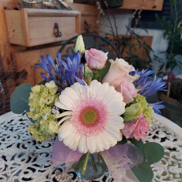 Bouquet of pink and white flowers in a glass vase with a lavender ribbon