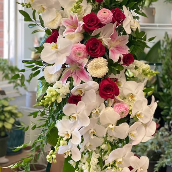 Tall floral standing spray with white orchids, red roses, and pink blooms