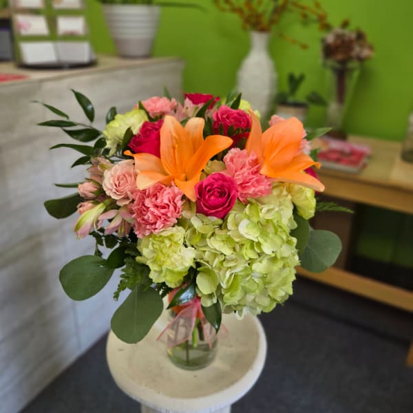 Bouquet of orange lilies, pink roses, and green hydrangeas in a glass vase