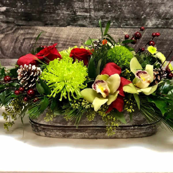 Low floral centerpiece with red roses, green mums, and orchids in a rustic container