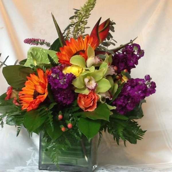 Bright mixed bouquet in a square glass vase with orange, purple, and green flowers