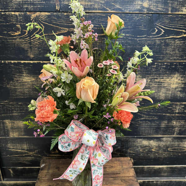 Mixed bouquet of peach and pink flowers in a glass vase with a floral ribbon