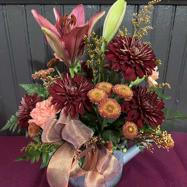 Bouquet of burgundy and peach flowers in a metal container with a large ribbon