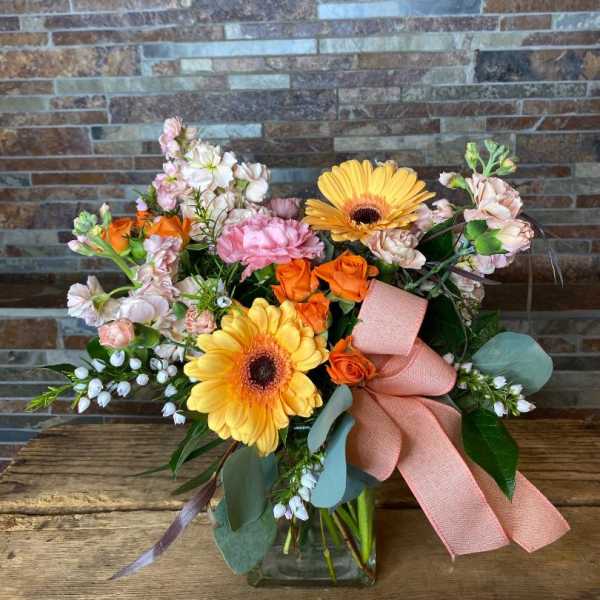 Bouquet of orange roses and yellow gerbera daisies in a glass vase with a pink ribbon