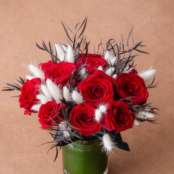 Red roses arranged in a glass vase with white fluffy accents