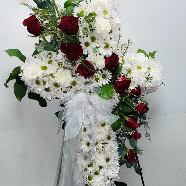 Cross-shaped floral spray with red roses and white daisies tied with a white bow
