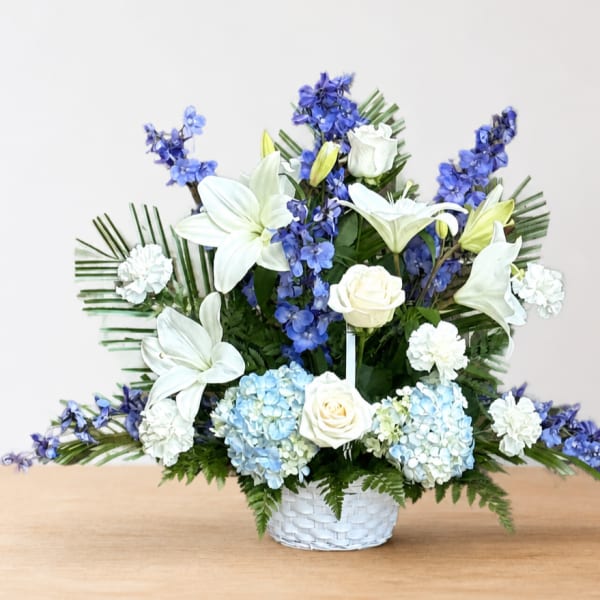 White lilies, roses, hydrangeas, and blue flowers in a white basket