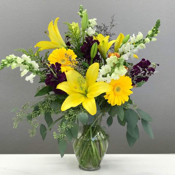 Yellow lilies and gerbera daisies in a glass vase