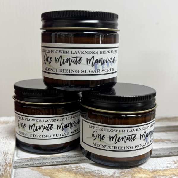 Three amber jars of lavender bergamot sugar scrub stacked on a wooden surface.
