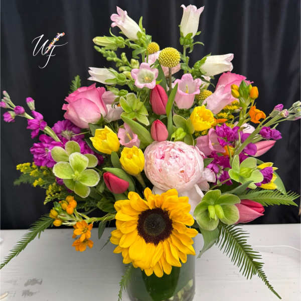 Mixed bouquet with sunflowers, pink roses, and tulips in a glass vase