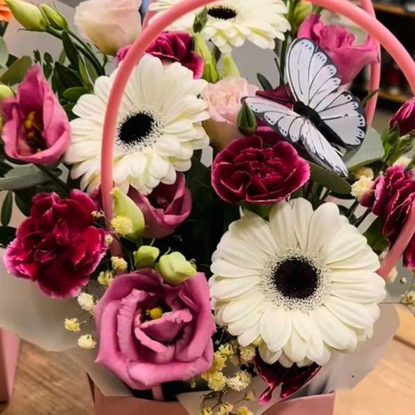Pink and white mixed flower arrangement with gerbera daisies and carnations in a pink handled box with a butterfly decoration.