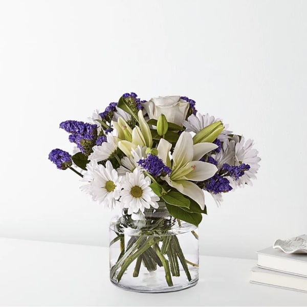 White lilies and daisies with purple filler in a clear glass vase