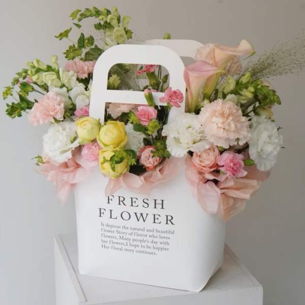 Pastel flower arrangement in a white gift bag with pink ribbon