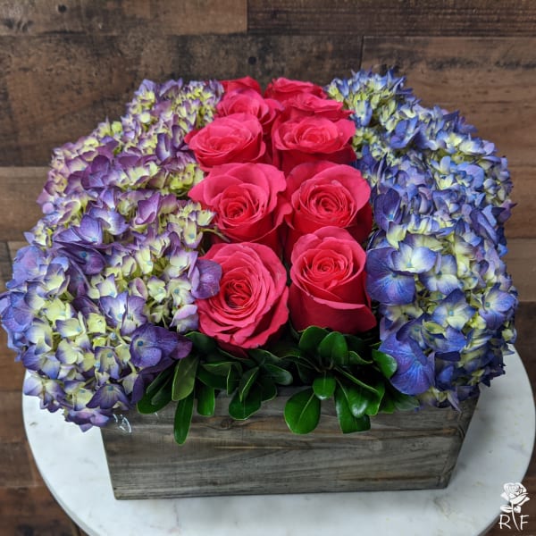 Pink roses surrounded by blue-purple hydrangeas in a wooden box