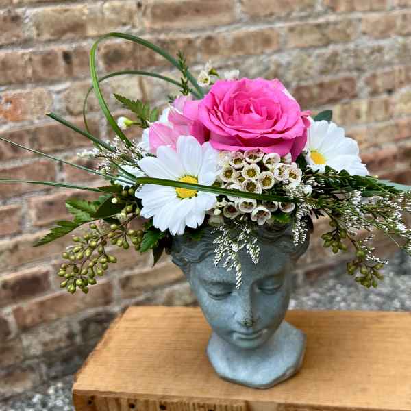 Pink rose arrangement in a blue face-shaped vase with white daisies