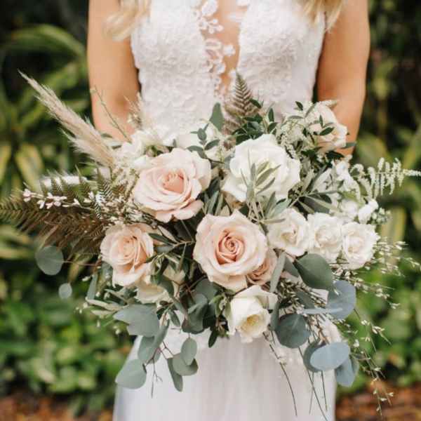 Bride holding a bouquet of blush and white roses with greenery