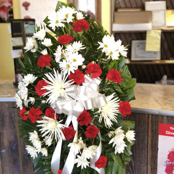 Standing floral wreath with red carnations and white daisies, tied with a white ribbon
