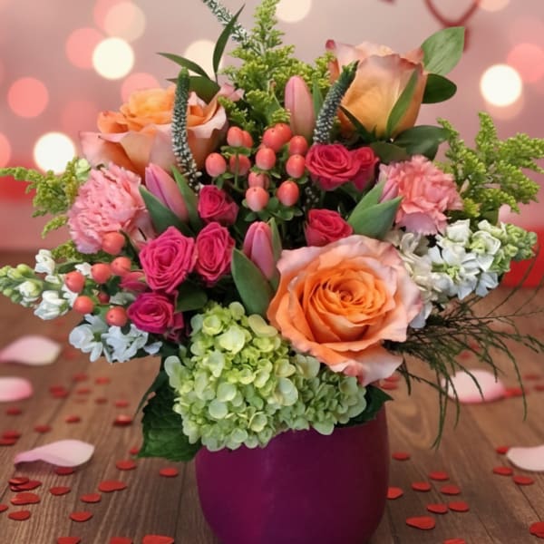 Pink and peach floral arrangement in a purple vase with heart decorations