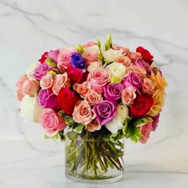 Mixed roses in pink, red, peach, white, and purple in a clear glass vase