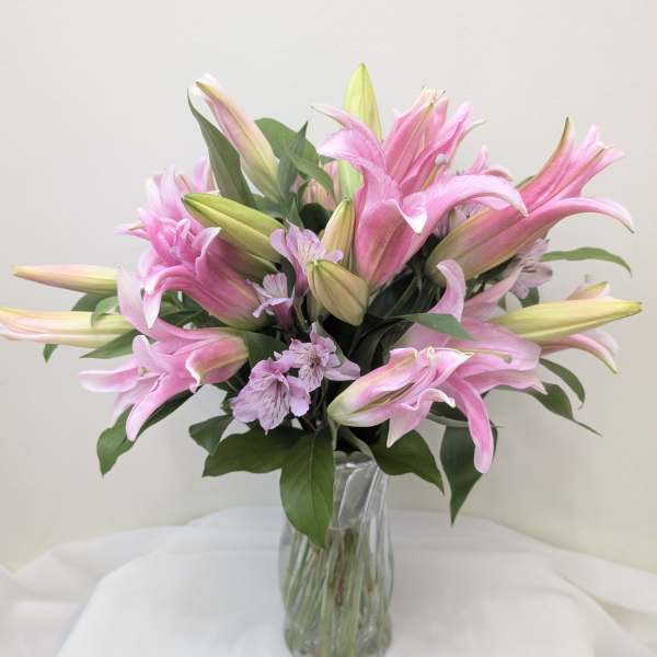 Pink lilies in a clear glass vase with small lavender flowers