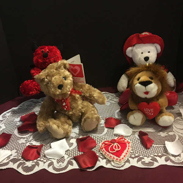 Three plush teddy bears with heart-themed accents on a lace cloth