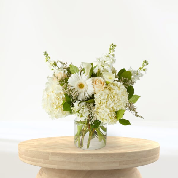 White floral arrangement in a clear glass vase on a wooden table