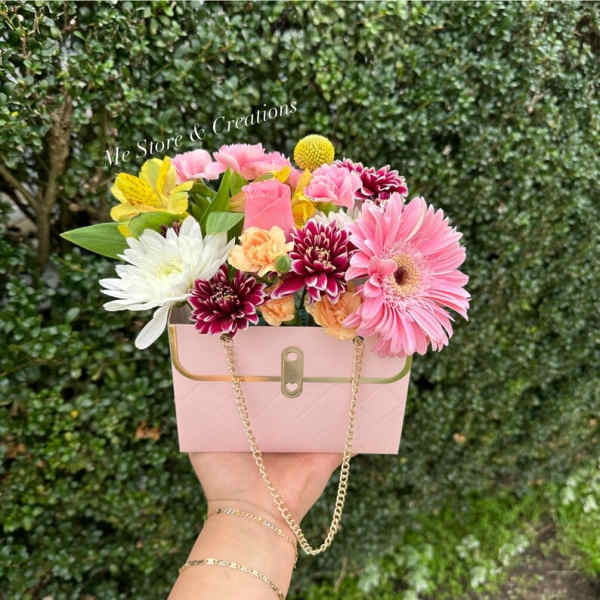 Pink floral arrangement in a small handbag-shaped box with a chain strap