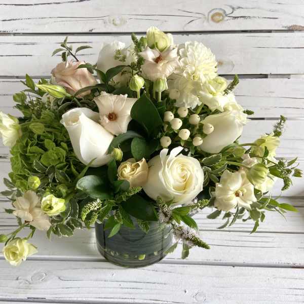 Round arrangement of white and cream flowers with soft green accents in a clear glass vase.