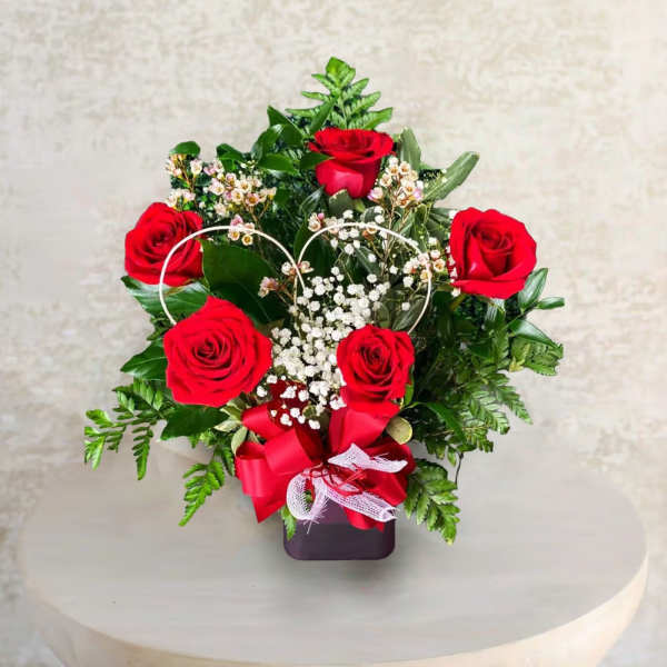 Red roses arranged in a heart-shaped design with baby's breath in a dark vase